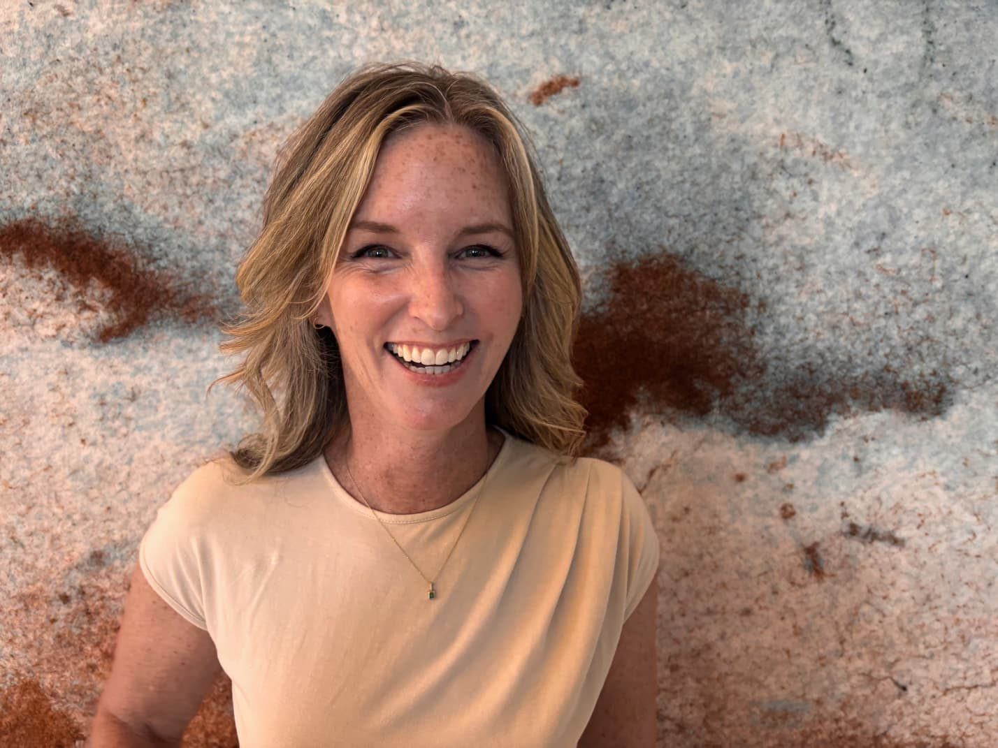 Heather MacLaren laughing in a tan top against a stone wall